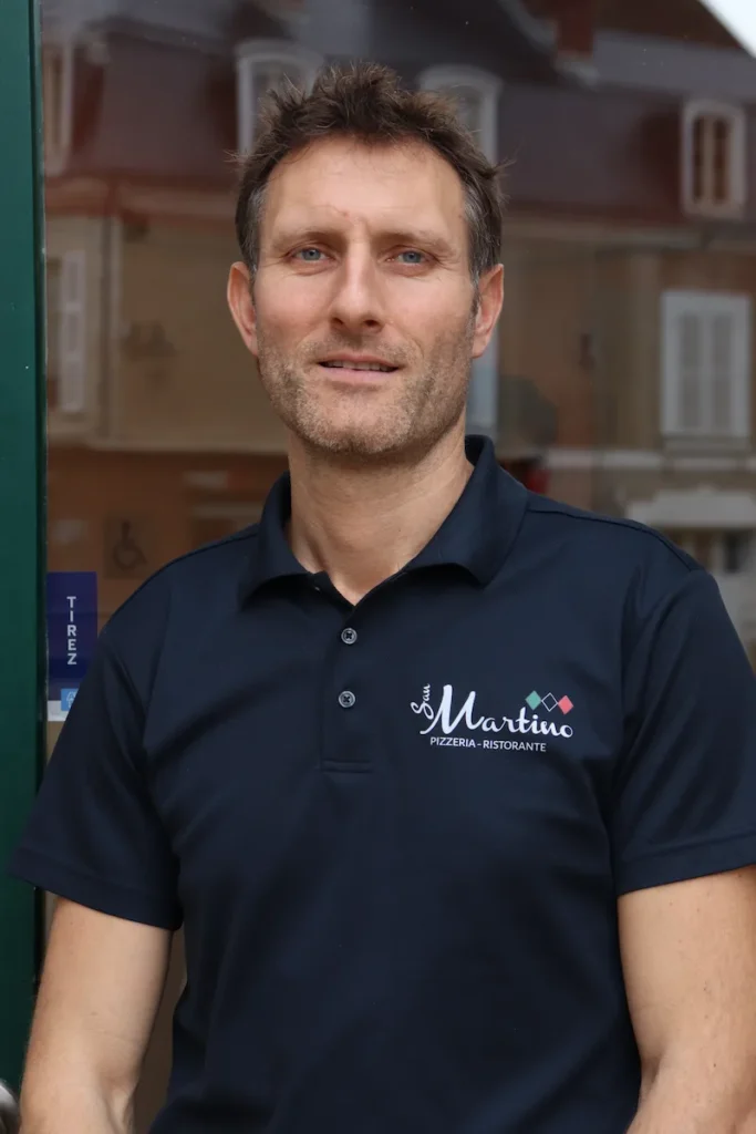 Man in navy polo outside pizzeria storefront